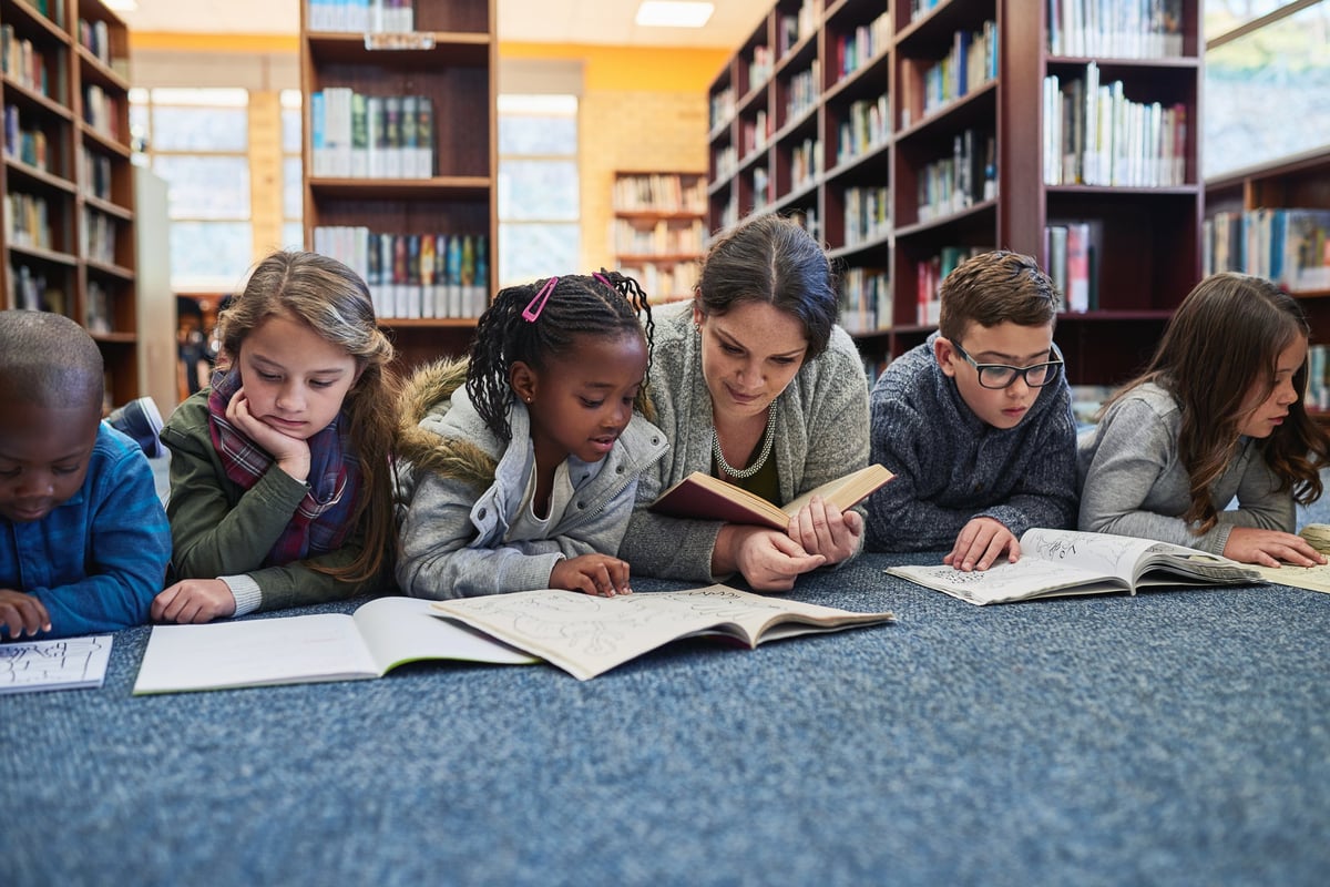 Group of elementary school kids and their teacher lying down while working in the library