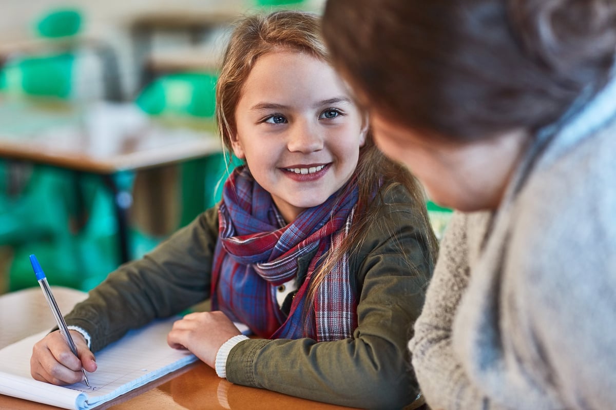 Elementary school girl getting help from her teacher with math in the classroom
