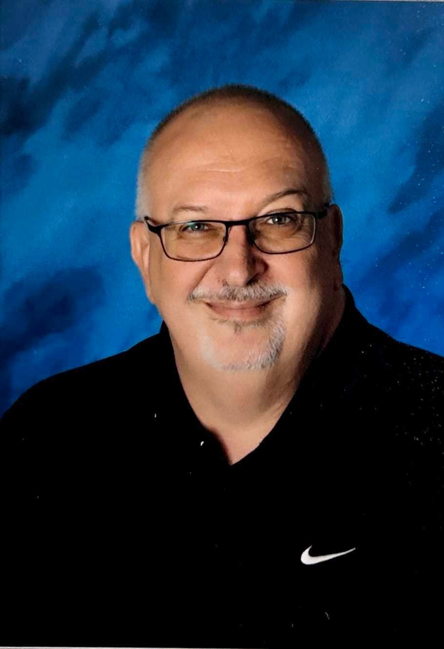 Professional headshot of a man wearing glasses and black Nike shirt against blue background