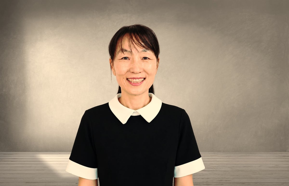 Smiling woman wearing a black and white collared shirt against a neutral gray background